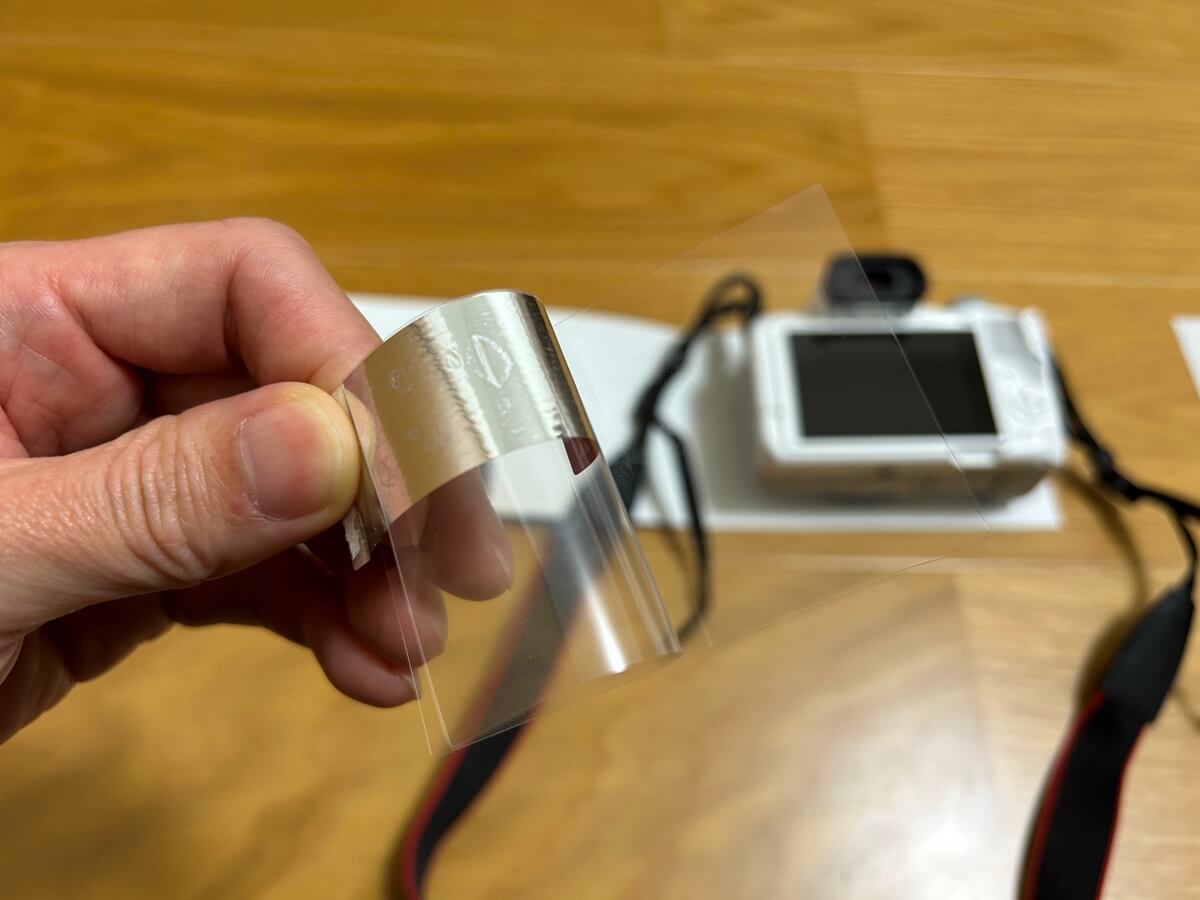 台紙シールを持ちながら、液晶保護フィルムを半分はがす